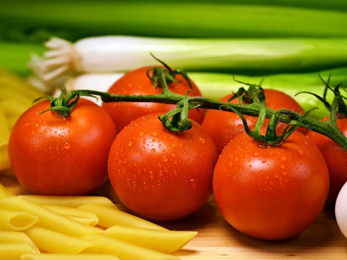 Vibrant tomatoes with pasta, green onions, and garlic create a healthy culinary scene.