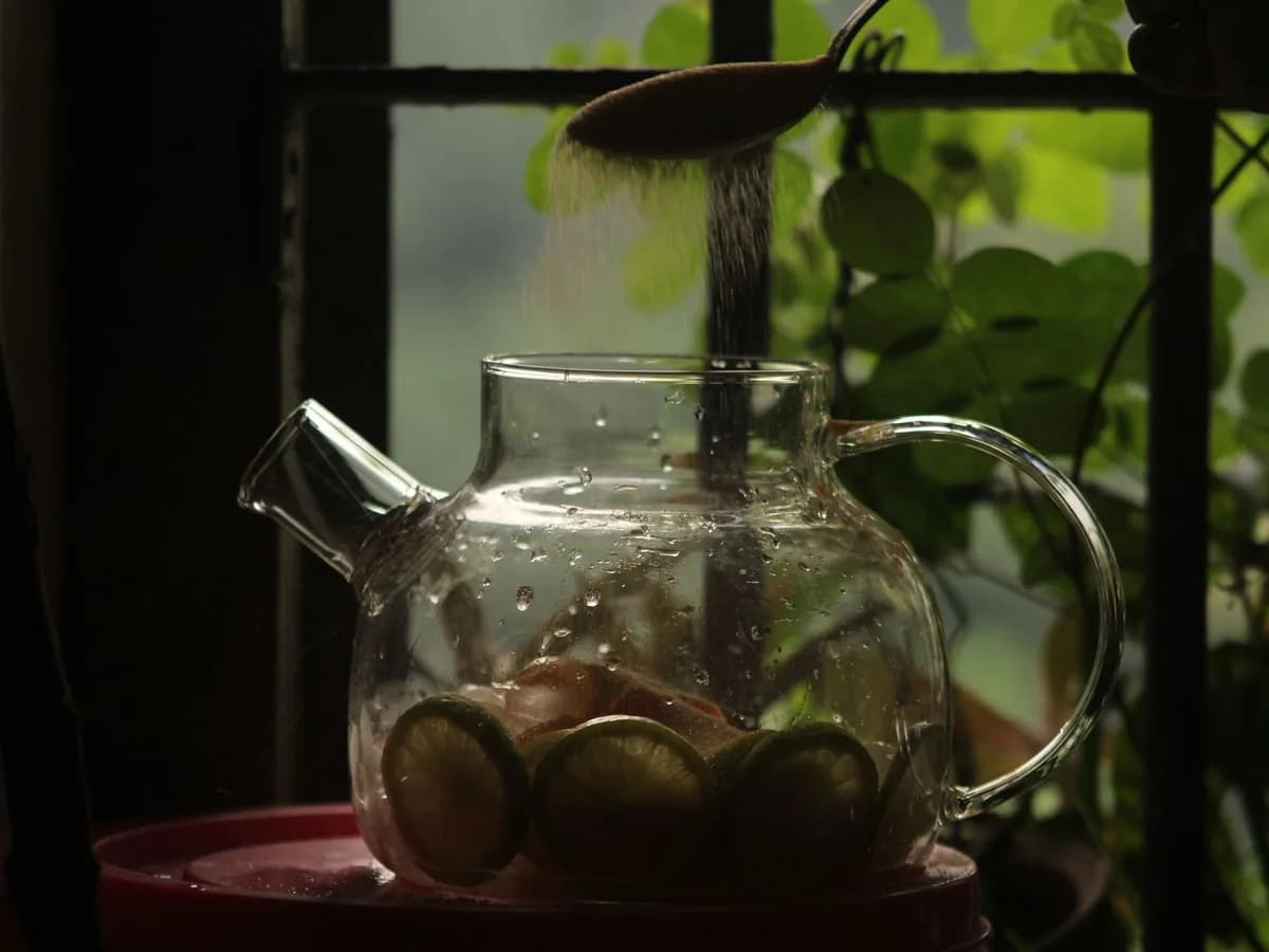 Glass teapot with lemon slices and sugar in soft window light, creating a cozy atmosphere.