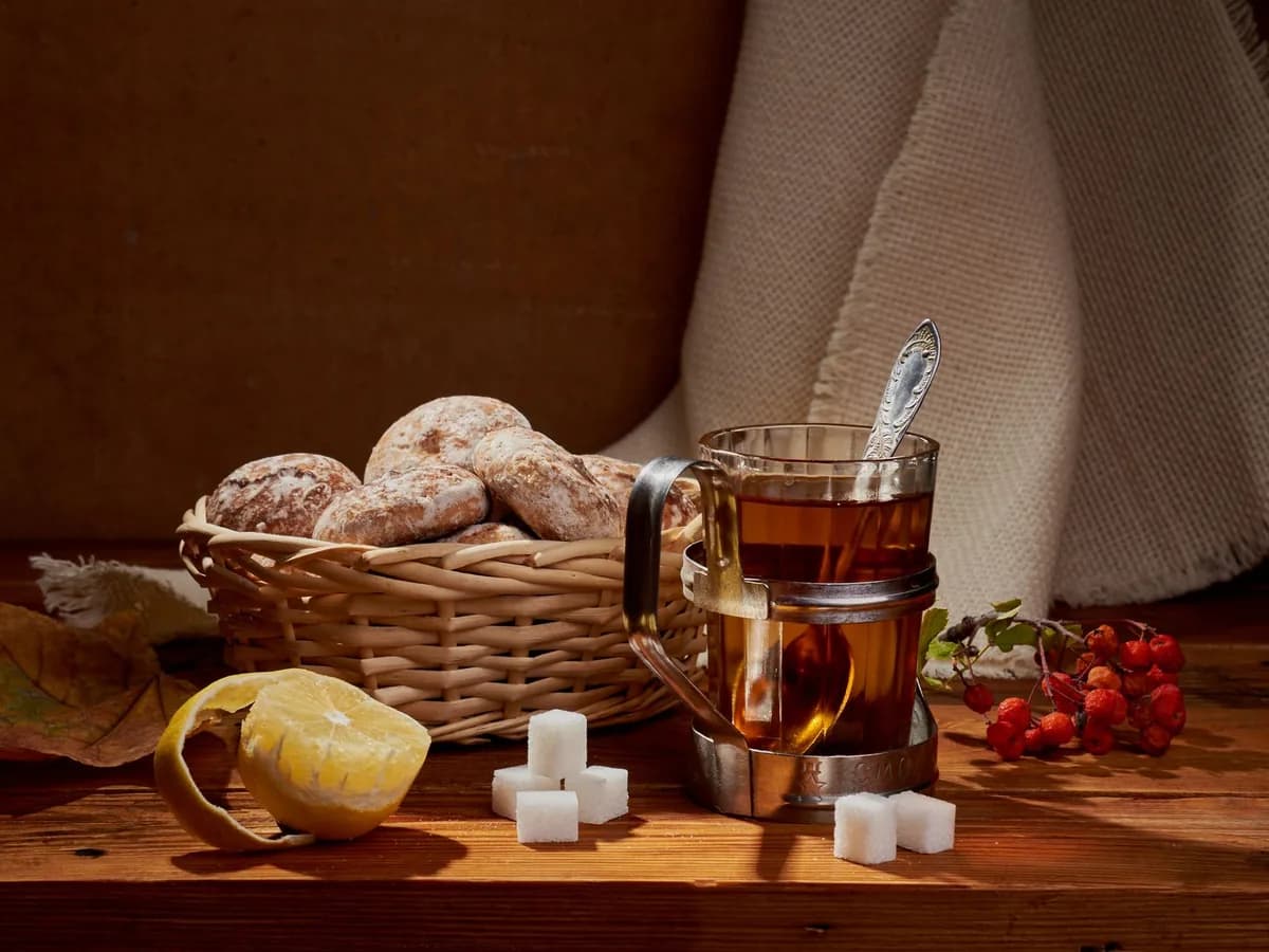 Cozy still life featuring tea, gingerbread cookies, lemon, sugar cubes, and berries.