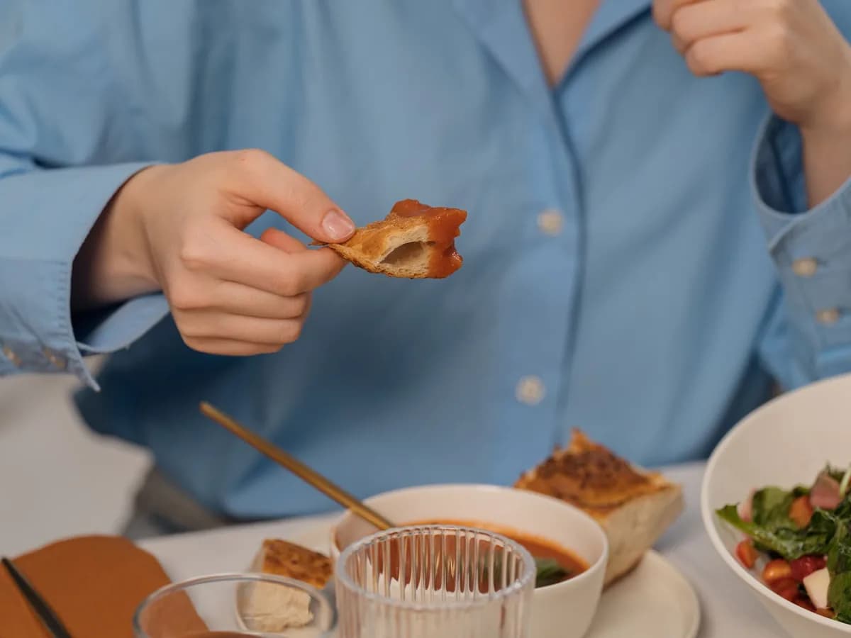 Close-up of a person enjoying bread with soup and salad, showcasing a casual dining setting.