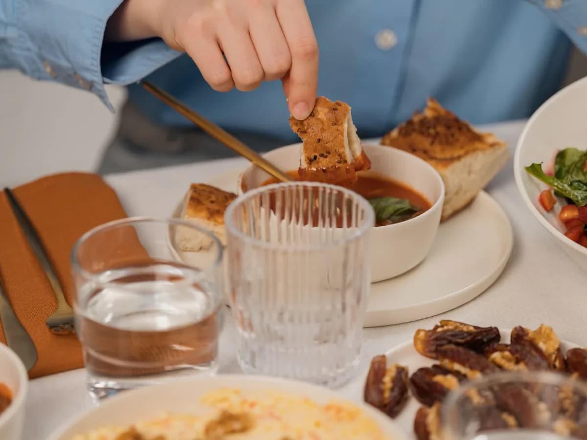 A warm dinner setup with soup, bread, salad, and glassware on a table.