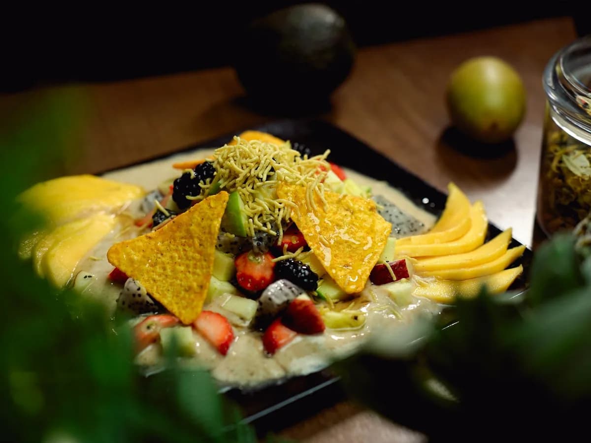 A vibrant fruit salad featuring mangoes, strawberries, papaya, nachos, and more, presented beautifully on a black plate.