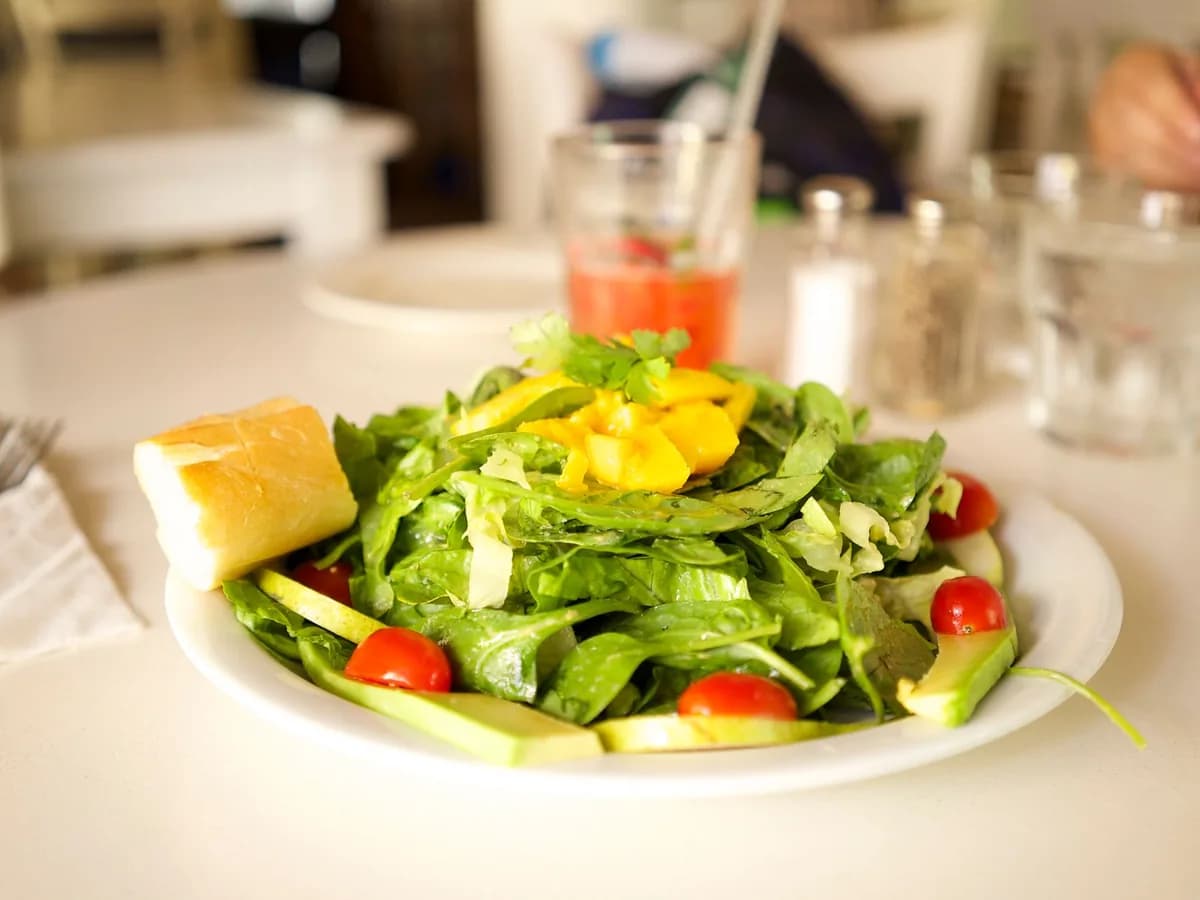 Healthy green salad with cherry tomatoes, lettuce, and mango on a white plate with bread.