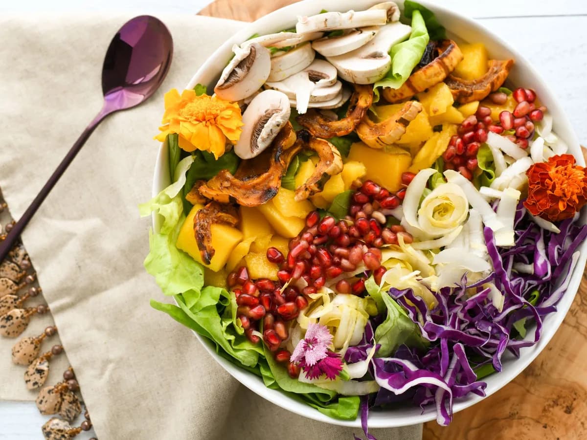 Colorful salad with fresh vegetables and fruits including pomegranate and mango, elegantly plated.