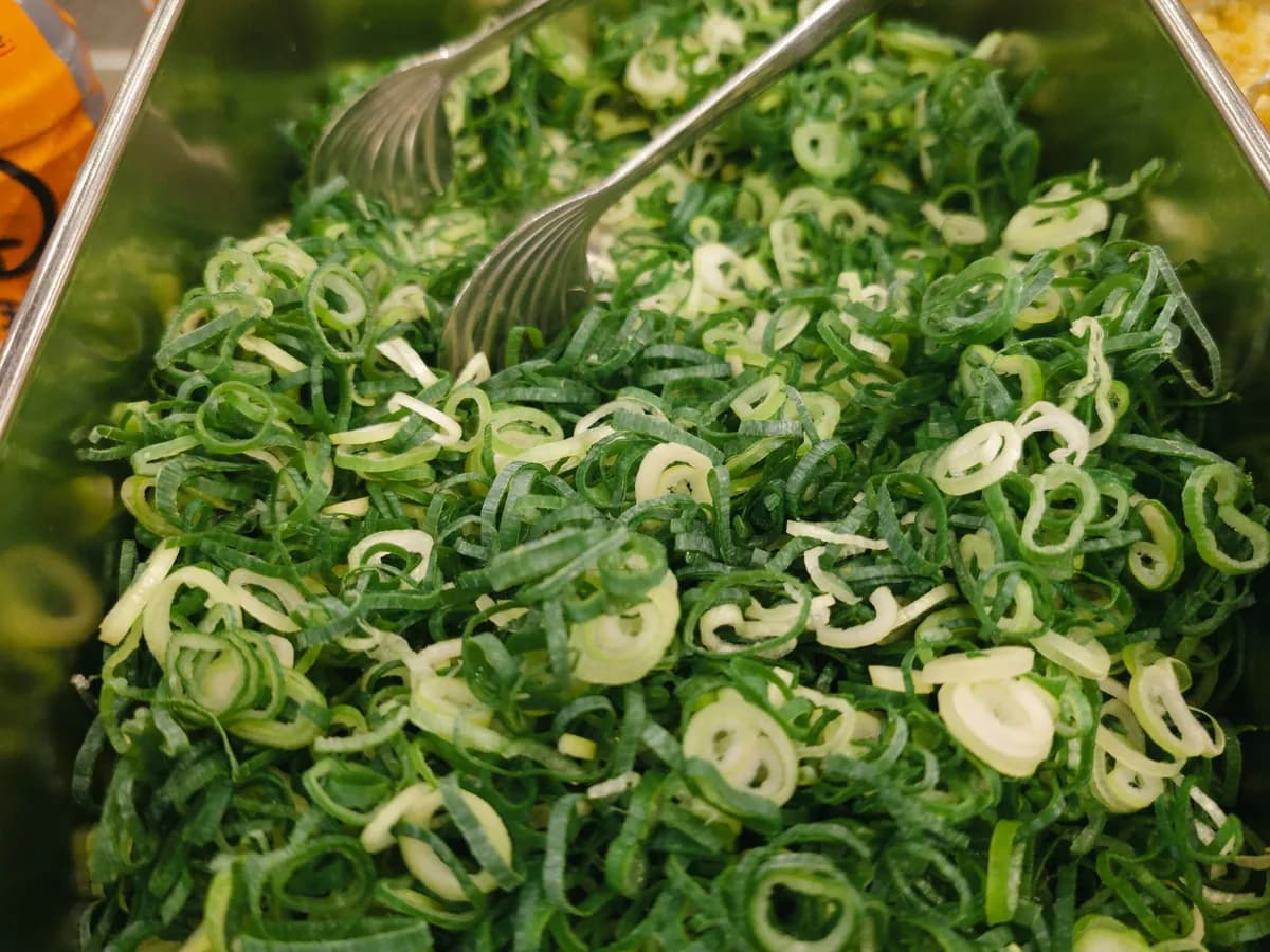 Close-up of fresh green onion slices in a metal container with tongs, ideal for salad or garnish.