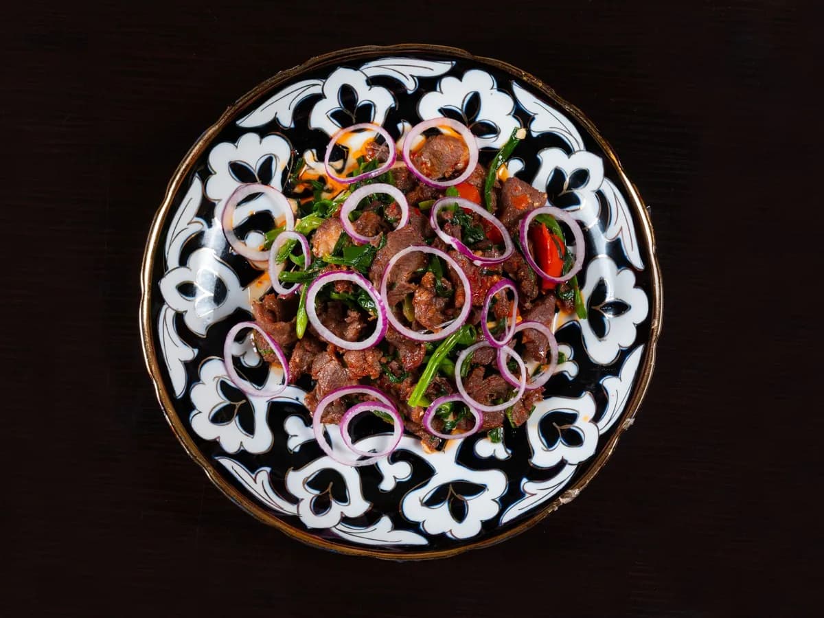 A vibrant meat salad with red onions on an ornate black-and-white plate.