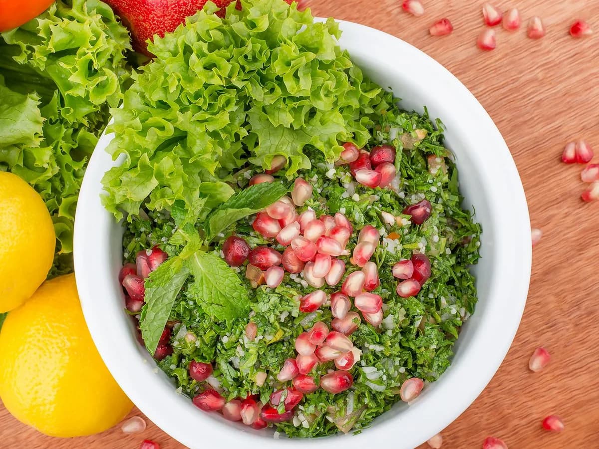 Delicious tabbouleh salad in a ceramic bowl topped with fresh pomegranate seeds and mint leaves.