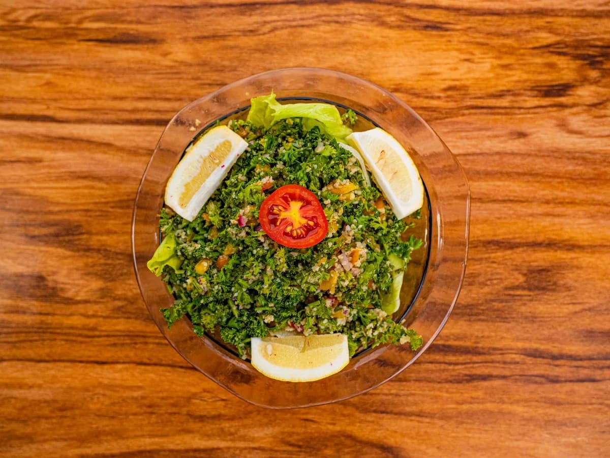 Top view of a vibrant tabbouleh salad garnished with tomato and lemon, set on a wooden surface.