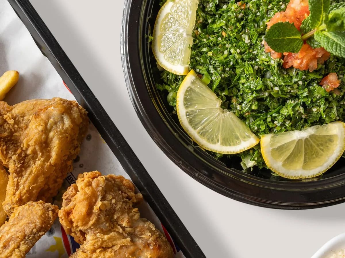 A delicious combination of crispy fried chicken with fries and vibrant tabbouleh salad garnished with lemon.