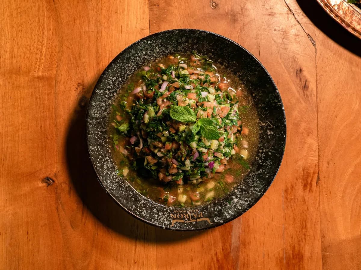 Delicious tabbouleh salad with fresh herbs in a dark bowl on a wooden table.