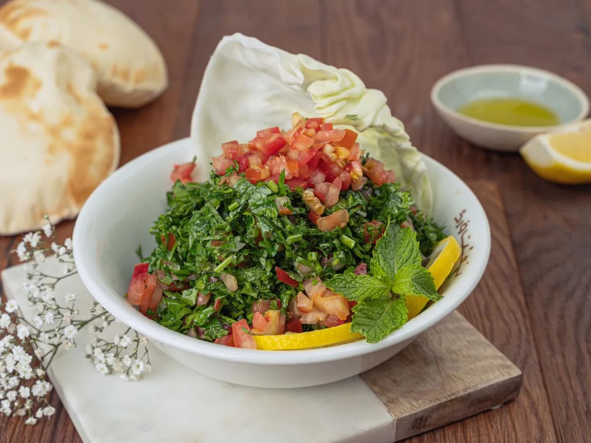 Vibrant tabbouleh salad with fresh ingredients, served with pita bread and lemon wedges.